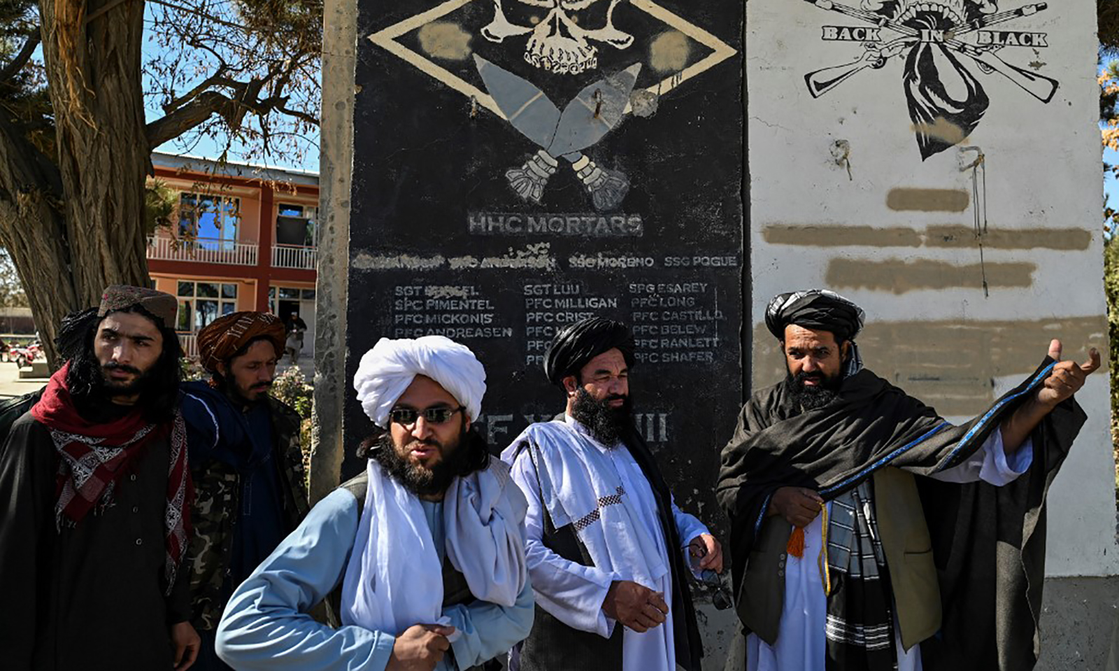 Quan chức Taliban đứng trước tường khắc tên lính Mỹ tham chiến tại tỉnh Ghazni, Afghanistan tháng 11/2021. Ảnh: AFP.