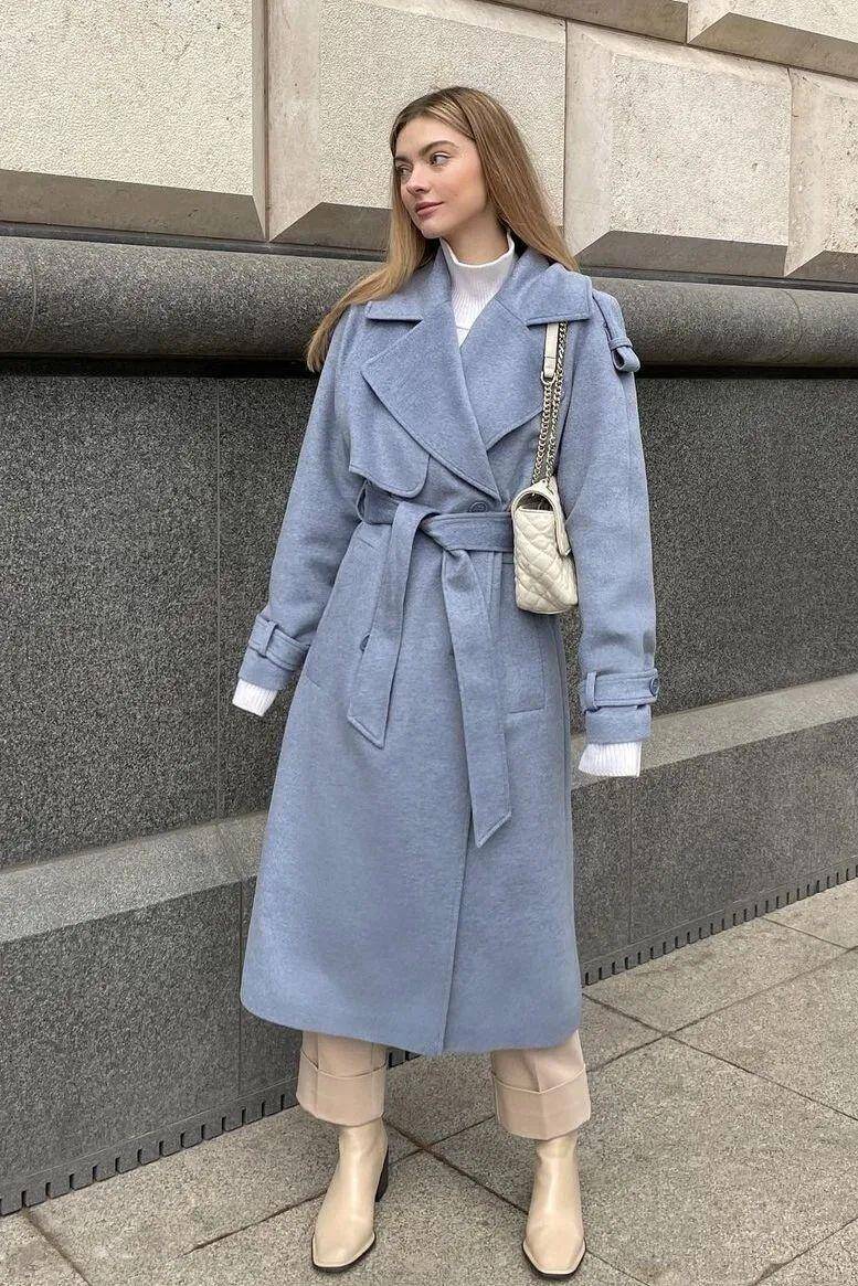 Áo trench coat xanh khói phủ ngoài lớp cổ lọ trắng tạo nên sự tương phản dịu dàng giữa tông lạnh và tông trung tính. Sắc xanh xám mang hơi thở hiện đại, còn trắng ngà giữ vai trò làm sáng gương mặt. 