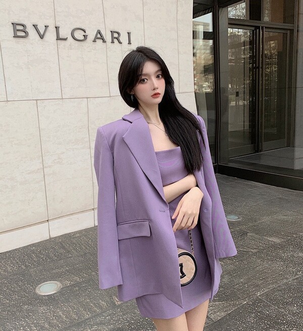 Bộ suit tím đồng bộ từ blazer đến váy ôm mang tinh thần power dressing đầy nữ tính. Sắc tím lavender tạo hiệu ứng vừa ngọt ngào vừa quyền lực, khác biệt hoàn toàn so với những gam trung tính quen thuộc nơi công sở. Phụ kiện tông nude giúp cân bằng thị giác, để màu tím thực sự trở thành tâm điểm.