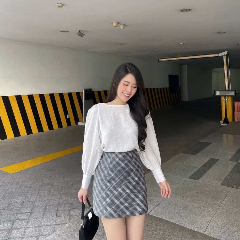 Áo blouse trắng tay bồng tạo vẻ thanh lịch, kết hợp với chân váy ngắn kẻ caro xám mang đến nét nữ tính và năng động.