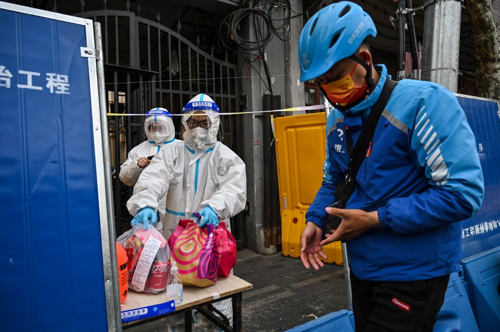 Nhân viên y tế mặc đồ bảo hộ nhận hàng hóa từ một người giao hàng sau rào chắn phong tỏa ở quận Tĩnh An, Thượng Hải, hôm 31/3. Ảnh: AFP