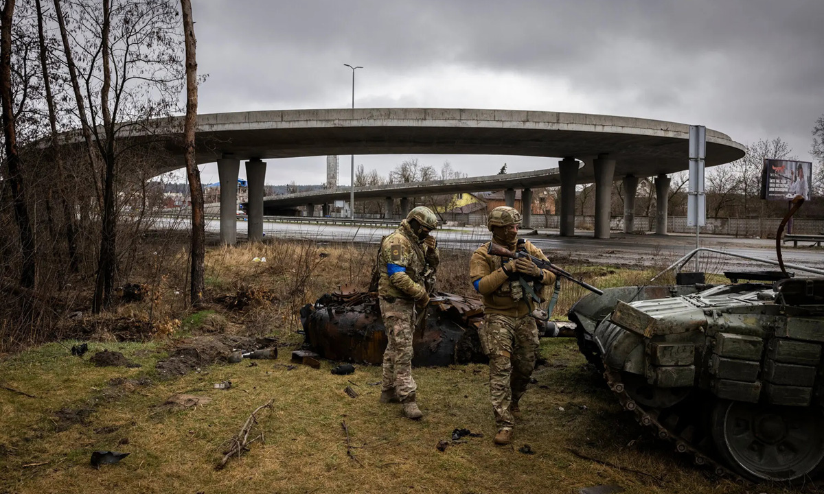 Hai lính Ukraine đứng cạnh một chiếc xe tăng bị hỏng ở ngoại ô Kiev hôm 2/4. Ảnh: NY Times.
