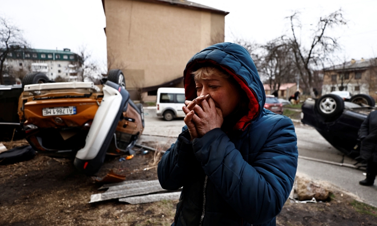 Người phụ nữ đứng cạnh những chiếc xe bị phá hủy ở Bucha, Ukraine, hôm 5/4. Ảnh: Reuters.