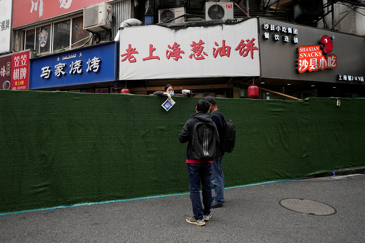 Một người bán thực phẩm giao dịch qua hàng rào phong tỏa ở Thượng Hải ngày 31/3. Ảnh: Reuters.