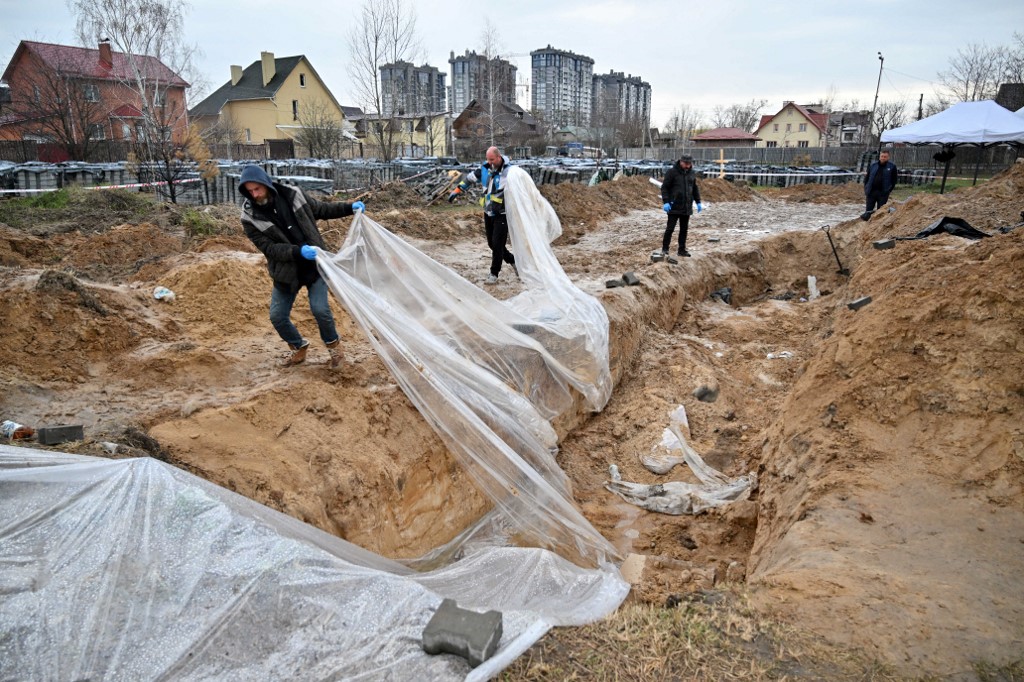 Người dân kéo nilon khỏi một ngôi mộ tập thể ở Bucha, gần Kiev, ngày 9/4. Ảnh: AFP