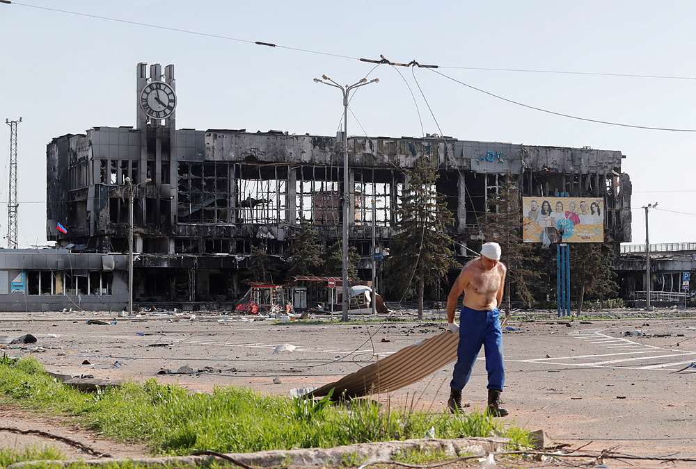 Người đàn ông kéo tấm kim loại gần tòa nhà ga đường sắt bị phá hủy do giao tranh ở thành phố Mariupol, Ukraine hôm 26/4. Ảnh: Reuters.