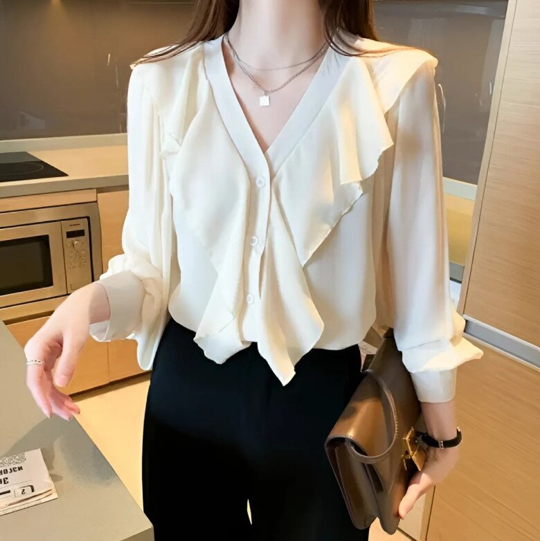 Chiếc sơ mi trắng kem với chất liệu voan lụa nhẹ, điểm nhấn bèo nhún cổ điển mang đến vẻ thanh lịch, nữ tính. Thiết kế cổ V và tay phồng nhẹ giúp tổng thể vừa hiện đại, vừa mềm mại, dễ phối đồ công sở lẫn dạo phố.
