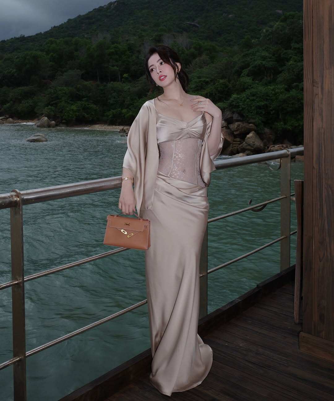 Chi Pu mở đầu với váy satin dáng dài màu champagne, kết hợp corset xuyên thấu có chi tiết ren tinh tế. Thiết kế ôm nhẹ giúp tôn dáng, trong khi áo choàng mỏng tạo cảm giác mềm mại. Outfit này thích hợp cho những dịp đặc biệt hay sự kiện sang trọng.
