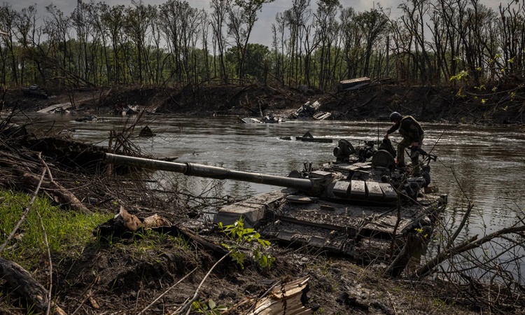 Một binh sĩ Ukraine kiểm tra một chiếc xe tăng Nga bị bỏ rơi bên sông Seversky Donets ngày 25/5. Ảnh: NY Times.