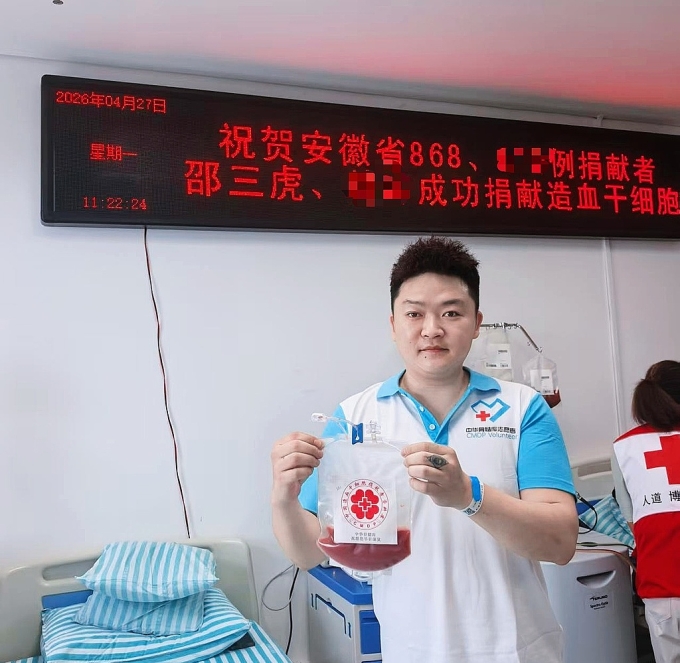 Thiệu Tam Hổ tại bệnh viện thành phố An Huy ngày 27/4, sau khi hiến tặng tế bào gốc thành công. Phía sau anh là bảng điện tử đề ngày tháng và lời chúc của bệnh viện. Ảnh: Sina