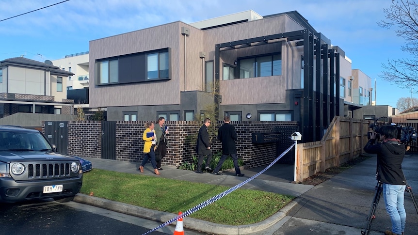 Detectives and crime scene tape outside an apartment block on a sunny day.