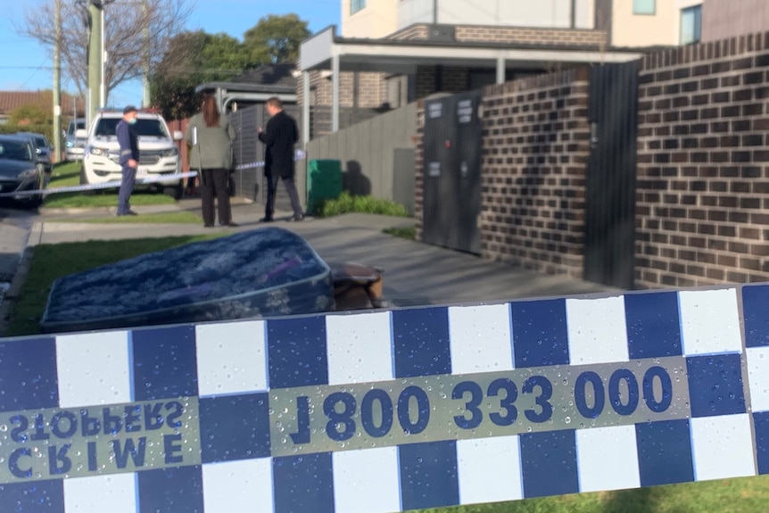 Crime scene tape in focus, with detectives out of focus in the background.