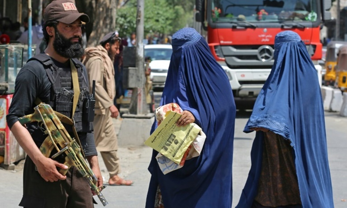 Phụ nữ Afghanistan đội khăn trùm kín đầu đi ngang qua một nhân viên an ninh ở Jalalabad. Ảnh: AFP
