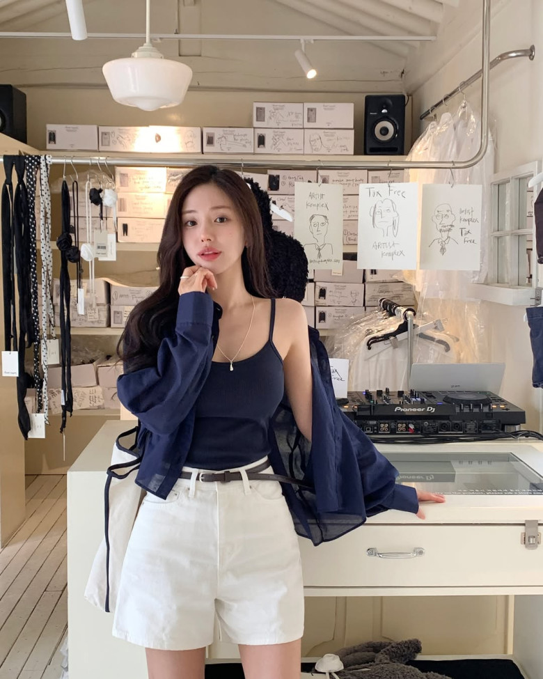 Nét quyến rũ tinh tế với áo hai dây đen gợi cảm, khoác ngoài sơ mi mỏng cùng tông màu. Quần shorts trắng cạp cao tôn dáng, kết hợp thắt lưng mảnh và túi xách trắng, tạo nên vẻ ngoài thanh lịch, phóng khoáng và đầy tự tin.