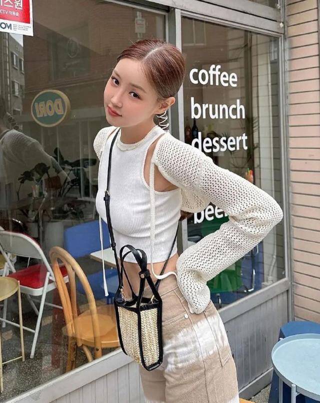 Phong cách trẻ trung, cá tính với áo crop-top trắng ôm sát, kết hợp áo khoác dệt kim dáng lửng độc đáo. Quần cạp cao màu be và túi cói mini đeo chéo tạo điểm nhấn ấn tượng, mang đến vẻ ngoài sành điệu và đầy cuốn hút.