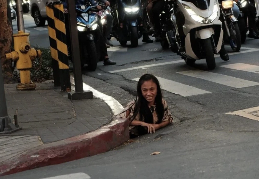Một phụ nữ người chuột bò ra từ lỗ cống ở Makati, Philippines, hôm 26/5. Ảnh: William Roberts