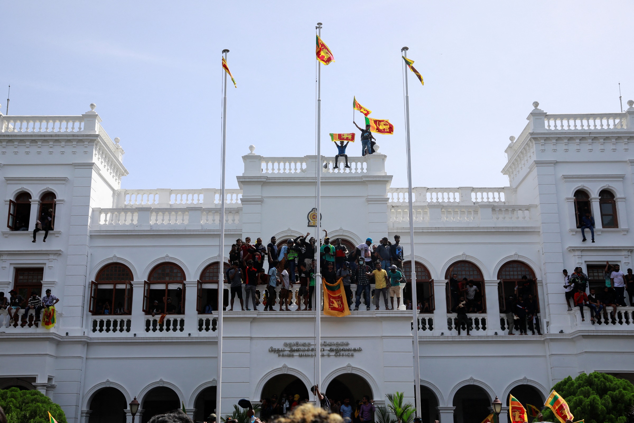 Protestors hold Sri Lankan flags as they stand on top of the office of Sri Lankas Prime Minister Ranil Wickremesinghe, amid the countrys economic crisis, in Colombo, Sri Lanka July 13, 2022. REUTERS/Adnan Abidi