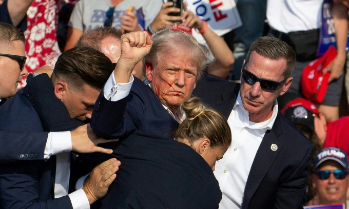 Ông Trump giơ nắm đấm thể hiện sự mạnh mẽ trong lúc được các mật vụ đưa rời sân khấu sau khi bị bắn tại Butler, Pennsylvania, ngày 13/7. Ảnh: AFP