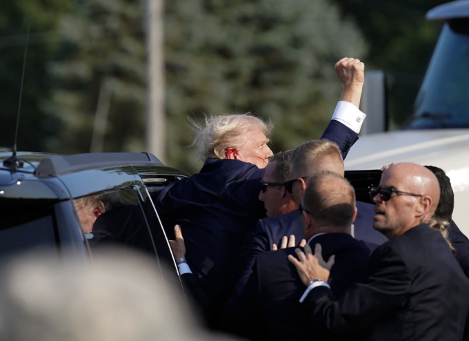 Ông Trump giơ cao nắm đấm lên trời khi được mật vụ hộ tống vào xe để rời hiện trường vụ ám sát ở Butler, bang Pennsylvania. Ảnh: WP