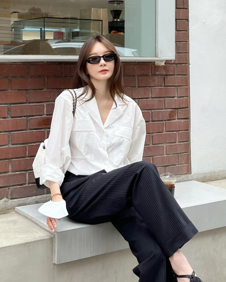Sự kết hợp giữa sơ mi trắng oversized và quần âu sọc mang đến vẻ đẹp thanh lịch, hiện đại. Chi tiết kính đen và túi vai tạo điểm nhấn sắc sảo, gợi phong thái “It Girl” Hàn Quốc đầy khí chất.