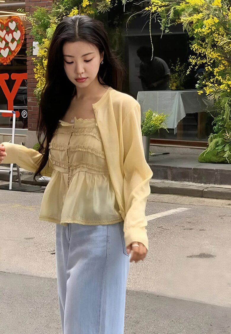 Áo blouse vàng có độ trong nhẹ tạo độ mềm mại cho phần thân trên, trong khi quần jeans xanh nhạt giúp outfit trở nên năng động hơn mà vẫn giữ được nét dịu dàng.