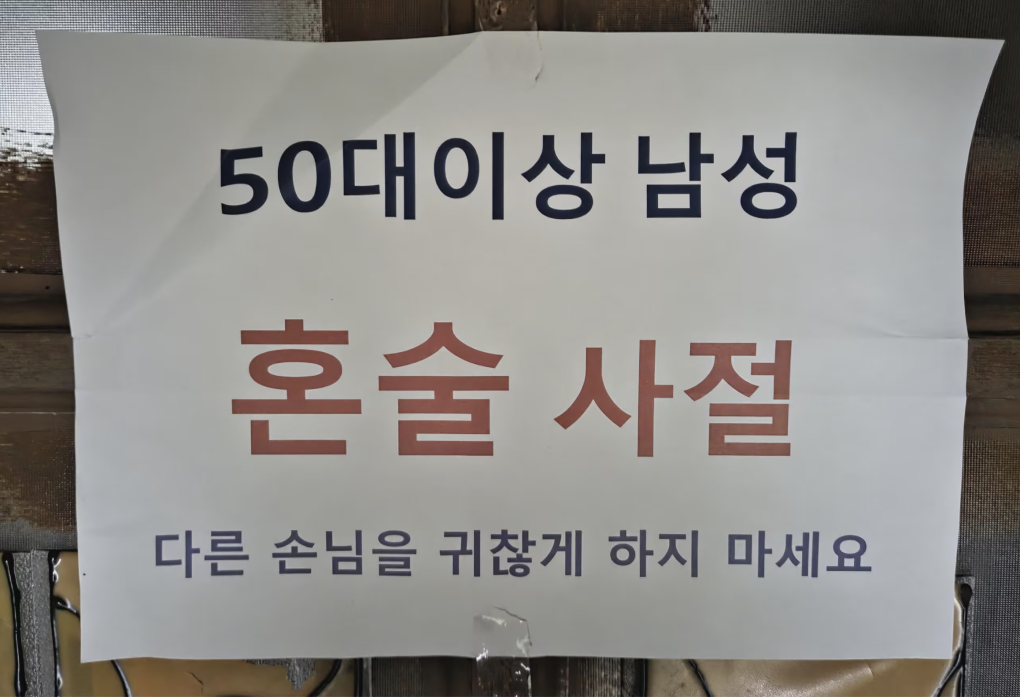 Một thông báo dán trước cửa của một quán bar ở Seoul năm 2025 Nam giới trên 50 tuổi, không được uống rượu một mình. Xin đừng làm phiền những khách khác. Ảnh: Jeong Sang-hyuk