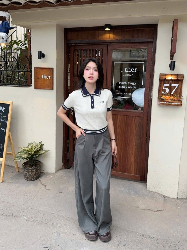 Áo len cổ polo dệt kim gam kem điểm xuyết viền đen, phối cùng quần ống suông xám ghi. Tông màu trung tính và phom dáng thoải mái tạo hiệu ứng thanh lịch, hiện đại, gợi nhớ phong cách “preppy chic” chuẩn Âu.