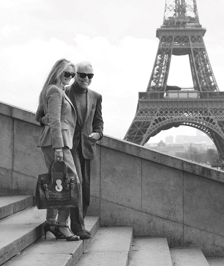Ricky Lauren cầm túi xách Ricky khi chụp ảnh cùng chồng cạnh tháp Eiffel. Phiên bản da cá sấu này hiện có giá 22.000 USD. Mẫu túi đặc trưng bởi phần khóa có dạng số tám được khắc chữ Ralph Lauren và đai phụ kiện hai bên. Ảnh: Ralph Lauren