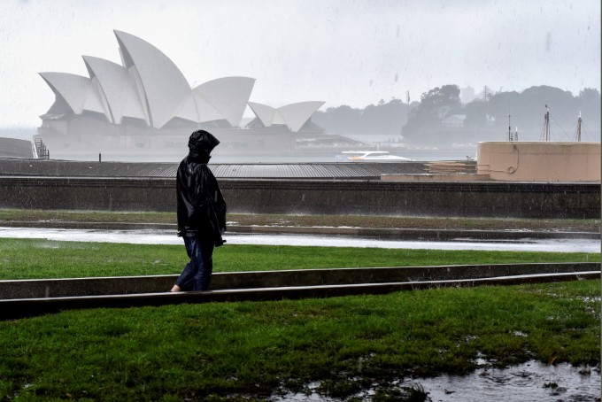 Một người phụ nữ đi bộ trước Nhà hát Opera giữa trời mưa ở Sydney ngày 6/10. Ảnh: AFP