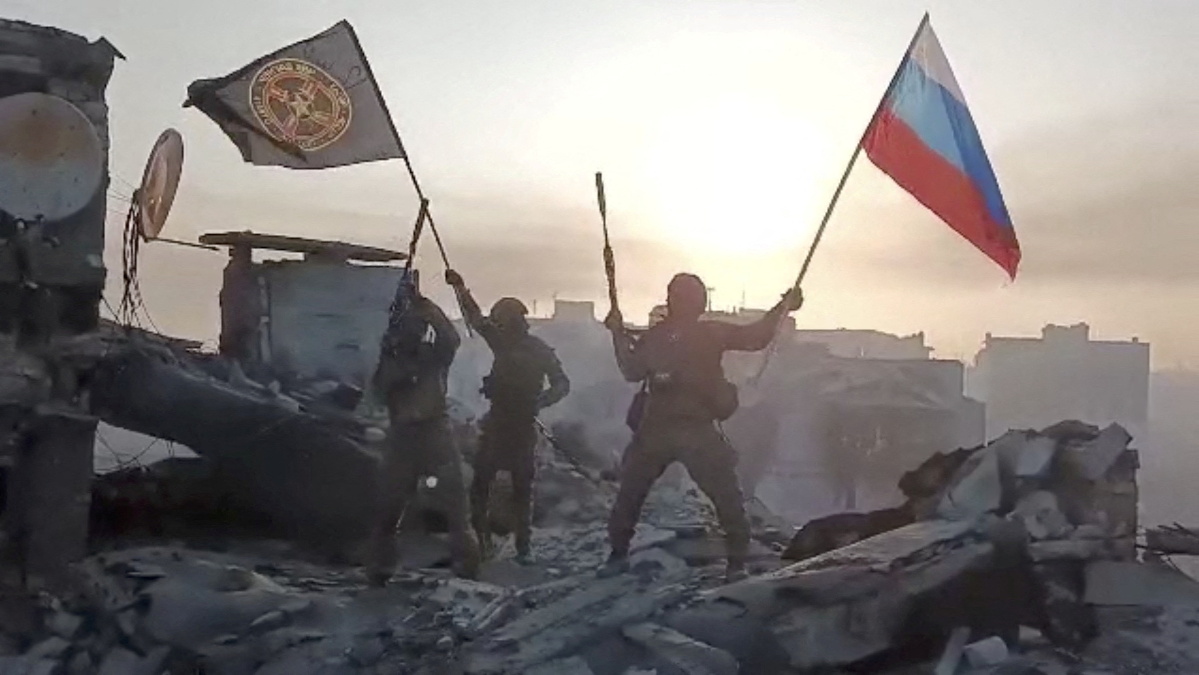 Thành viên lực lượng Wagner giương cao cờ Nga và cờ Wagner trên một tòa nhà đổ nát không rõ địa điểm trong đoạn video công bố ngày 20/5. Ảnh: Reuters