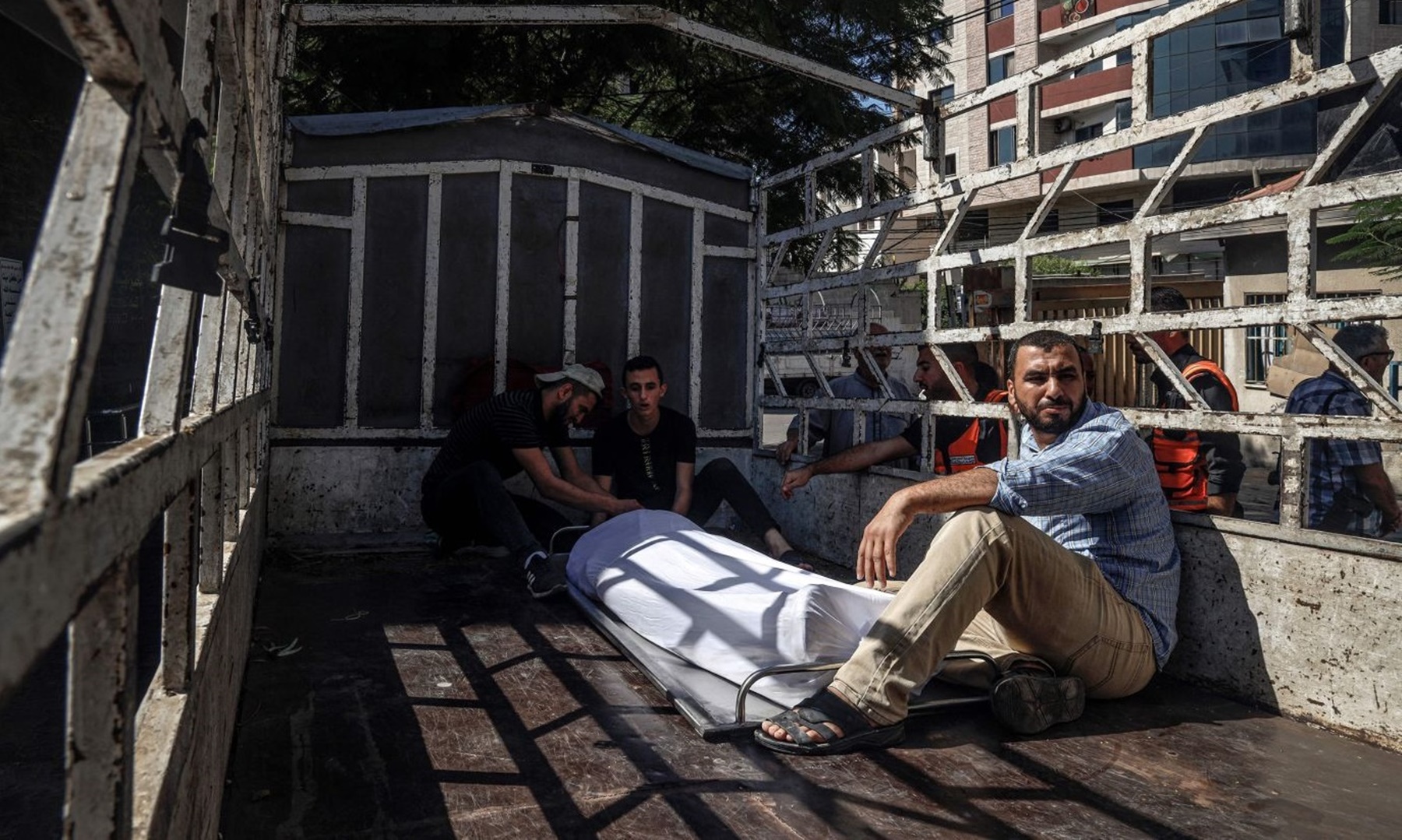 Những người đàn ông ngồi cạnh thi thể của một chiến binh Palestine bên ngoài một bệnh viện ở Dải Gaza hôm 7/10. Ảnh: AFP