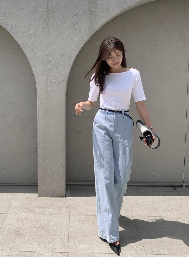 Áo thun trắng basic kết hợp cùng quần jeans ống rộng xanh nhạt - công thức tối giản nhưng chưa bao giờ lỗi mốt. Thắt lưng đen nhấn nhá vòng eo, phối cùng giày mũi nhọn và clutch kẹp tay, biến một outfit casual thành phong cách street chic hiện đại.