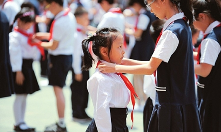 Một học sinh lớp 6 chỉnh lại  khăn quàng đỏ cho một học sinh lớp một tại Trường Tiểu học Thực nghiệm Sơn Tây, hồi năm 2018. Ảnh: Shanxi Daily.