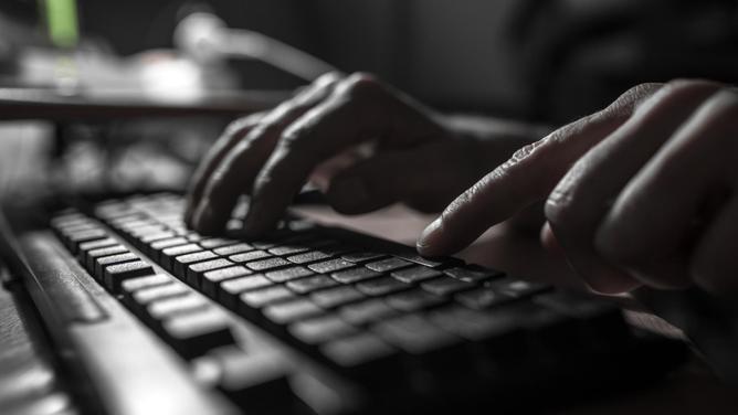 Fingers pressing on a computer keyboard in the dark .