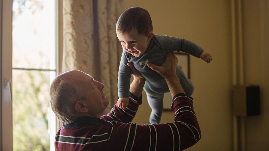 A man holds up a cute, smiling baby.