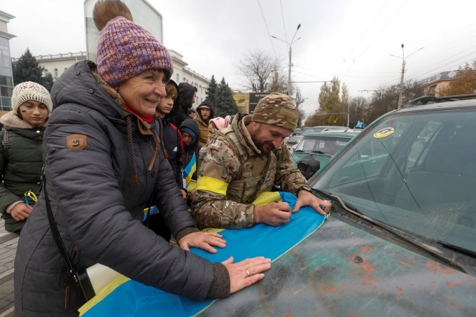 Binh sĩ Ukraine đứng cạnh người dân ký vào quốc kỳ ở thành phố Kherson hôm 13/11. Ảnh: Reuters.