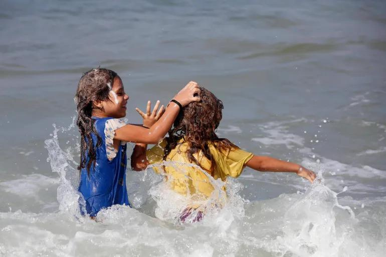 Hai em nhỏ giúp nhau gội đầu trên bãi biển Deir al-Balah, miền nam Gaza. Ảnh: Al Jazeera
