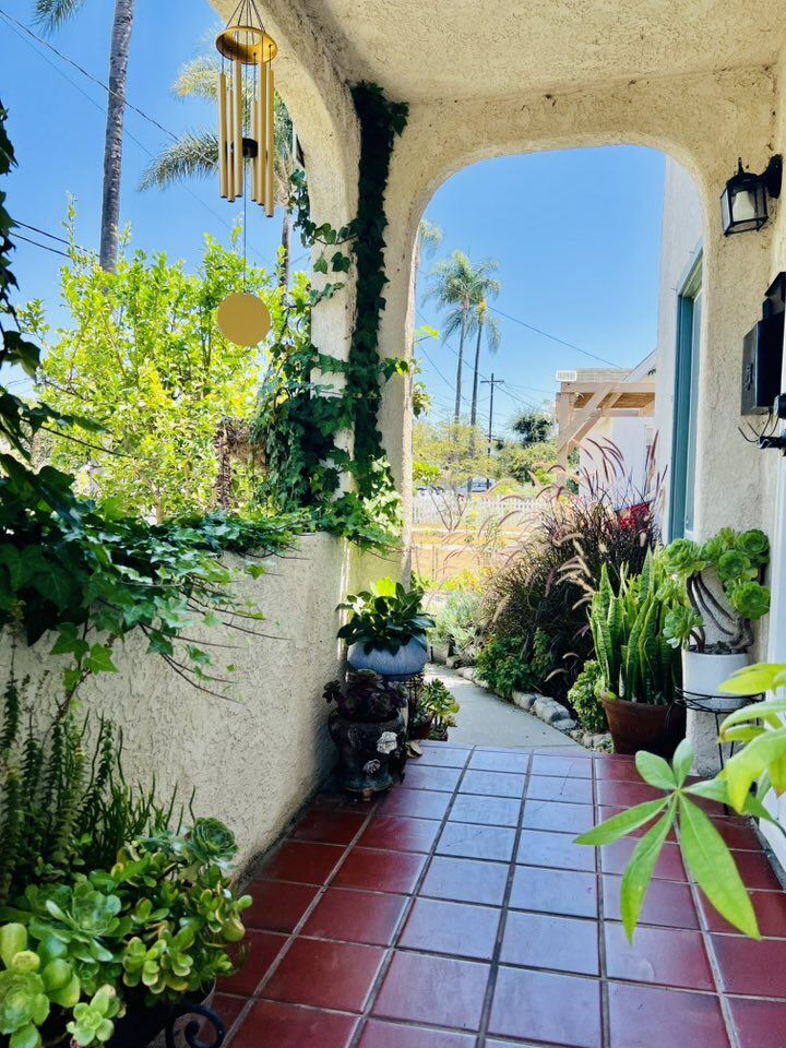 Dãy hành lang lát gạch đỏ dẫn vào nhà được tô điểm bởi các chậu cây phong phú. Những loại cây như trầu bà, sen đá, cỏ lan chi và cả dây thường xuân bò lên cột nhà tạo thành một bức tranh xanh dịu mắt.