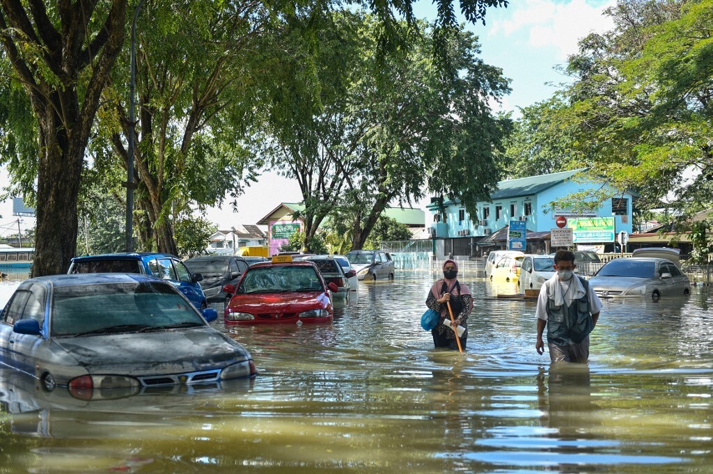 Người dân lội qua khu vực bị ngập lũ ở thành phố Shah Alam, bang Selangor, Malaysia hôm 21/12. Ảnh: AFP.