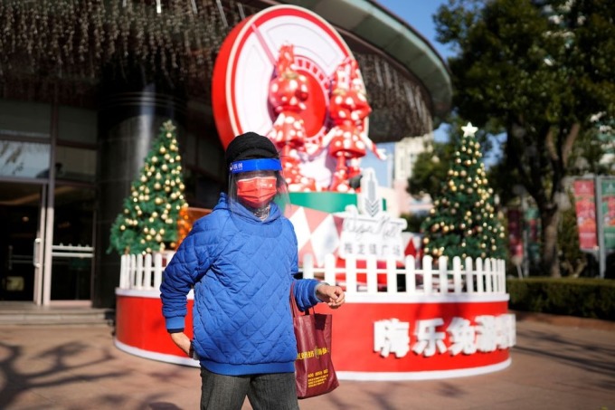 Một phụ nữ đeo mặt nạ chống giọt bắn đi dạo trước một trung tâm mua sắm ở Thượng Hải ngày 22/12. Ảnh: Reuters