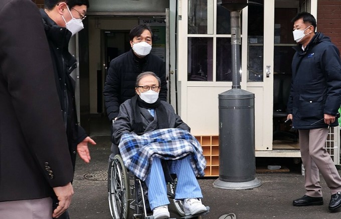 Cựu tổng thống Hàn Quốc Lee Myung-bakngồi xe lăn rời Bệnh viện Đại học Quốc gia Seoul tháng 2/2021, trước khi được đưa đến đến trại giam ở Anyang, phía nam thủ đô Seoul. Ảnh: Yonhap.