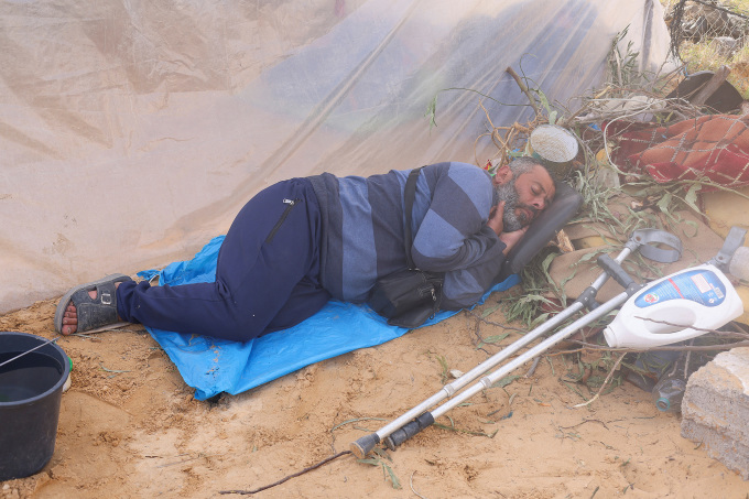 Một người đàn ông Palestine trải bạt nằm ngủ dưới nền đất tại trải tị nạn ở Rafah, miền nam Dải Gaza, ngày 10/12. Ảnh: Reuters