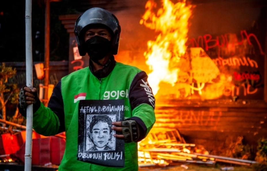 Người đàn ông mặc đồng phục của công ty xe công nghệ, cầm chân dung của tài xế bị xe cảnh sát cán chết trong cuộc biểu tình trước trụ sở cảnh sát Jakarta ngày 29/8. Ảnh: AFP