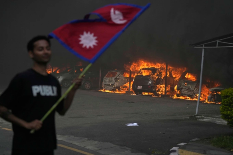 Một người biểu tình cầm cờ Nepal đứng gần các phương tiện đang bị đốt cháy ở thủ đô Kathmandu ngày 9/9. Ảnh: AP