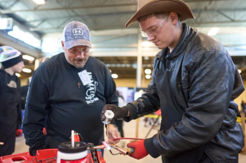 Daniel Friesen (mặc áo da) học hàn ống đồng tại hội chợ nghề ở Ontario, Canada. Ảnh: Globe and Mail